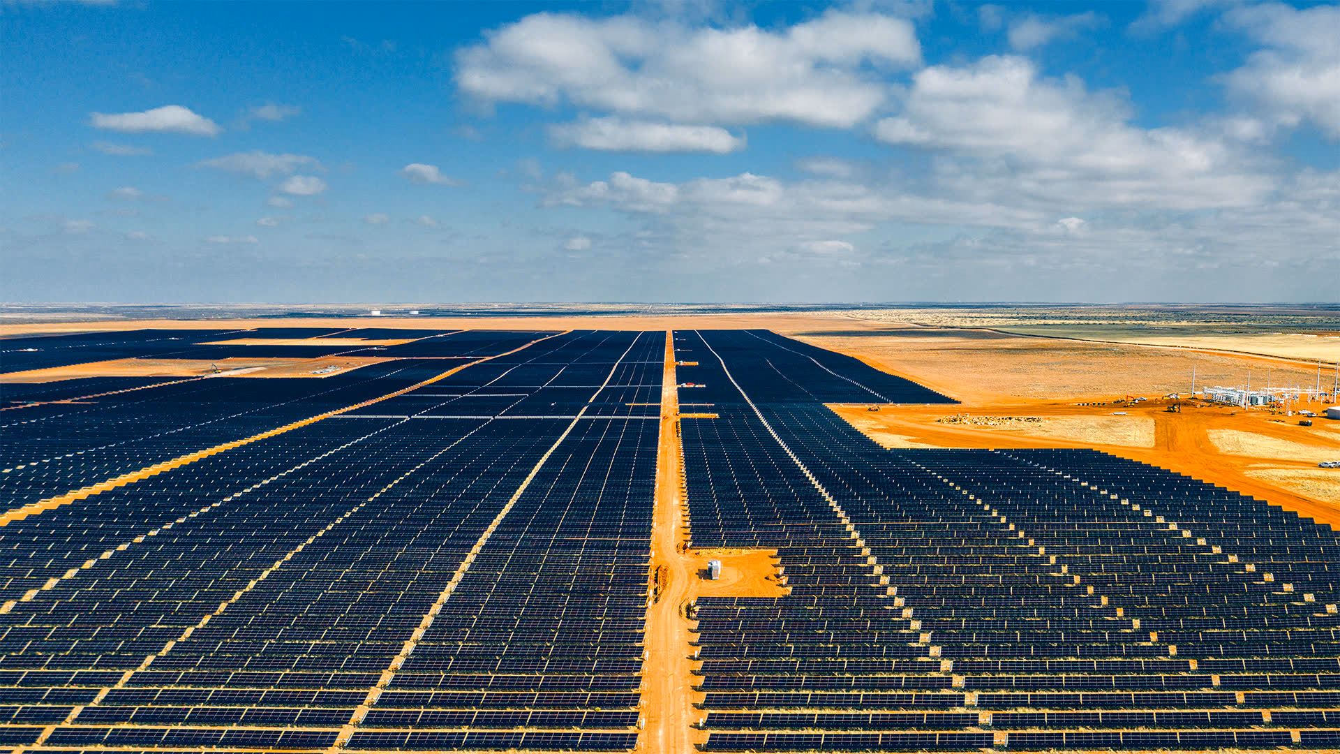 High aerial of a vast desert solar farm on NX trackers, service roads cutting through the array
