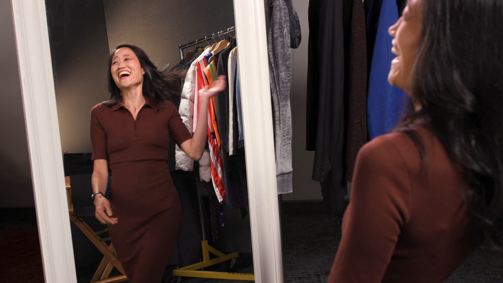 A guest in a burgundy dress laughs mid-gesture at her reflection in the wardrobe mirror