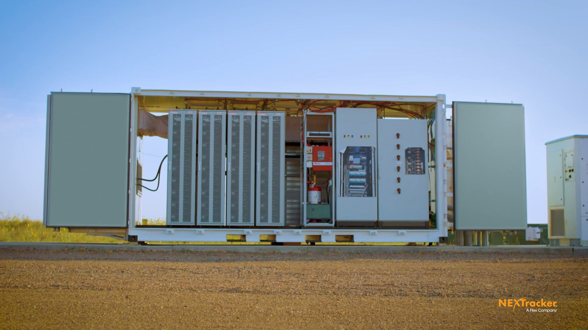 A battery storage container with its doors open, battery racks and controls visible, staged in a field
