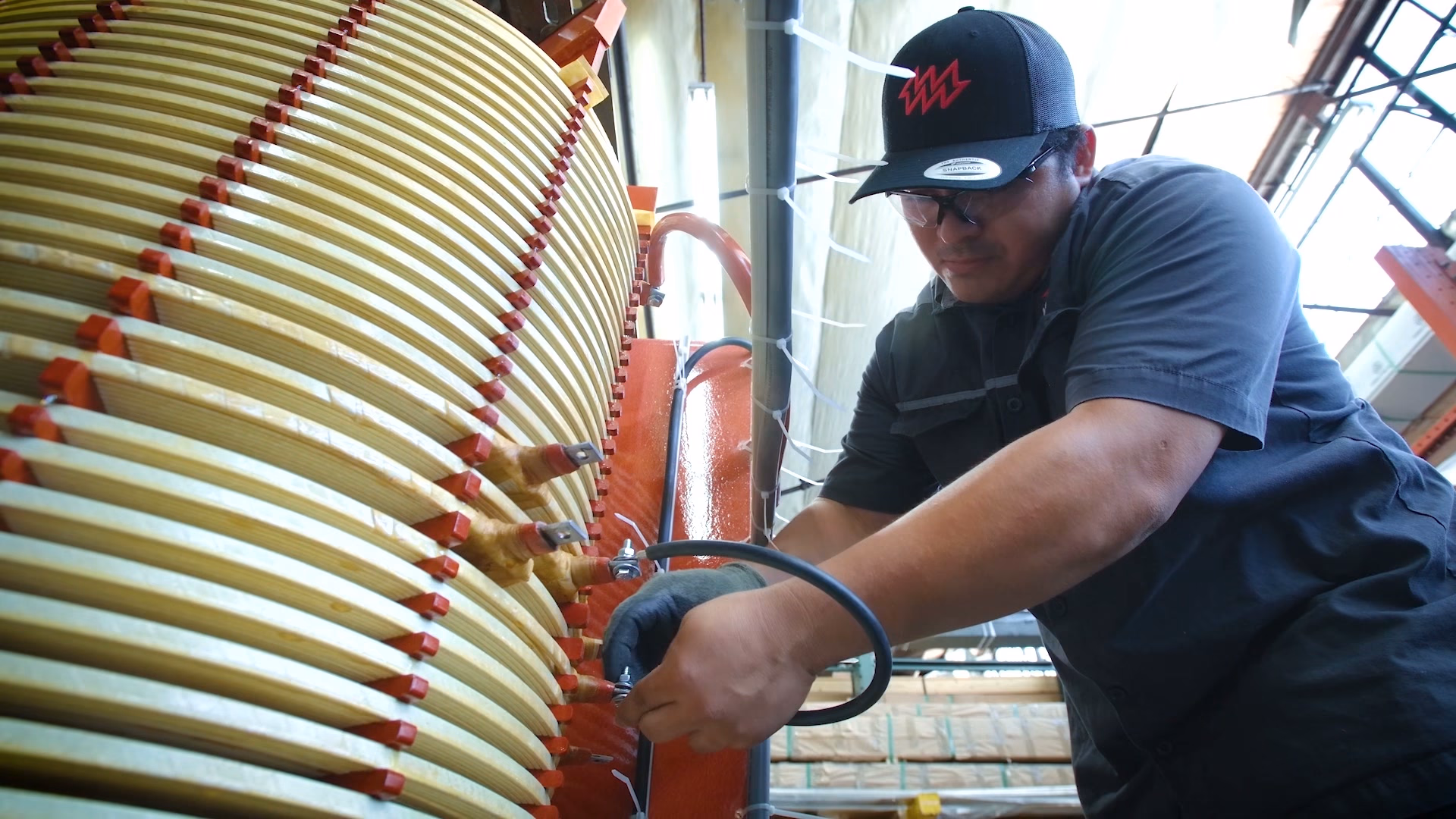A worker in a cap bending a coil lead on a transformer winding stack