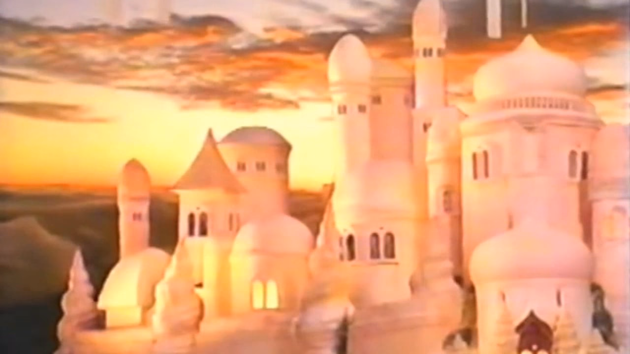 A castle city of cream domes and spires against a sunset sky, windows glowing