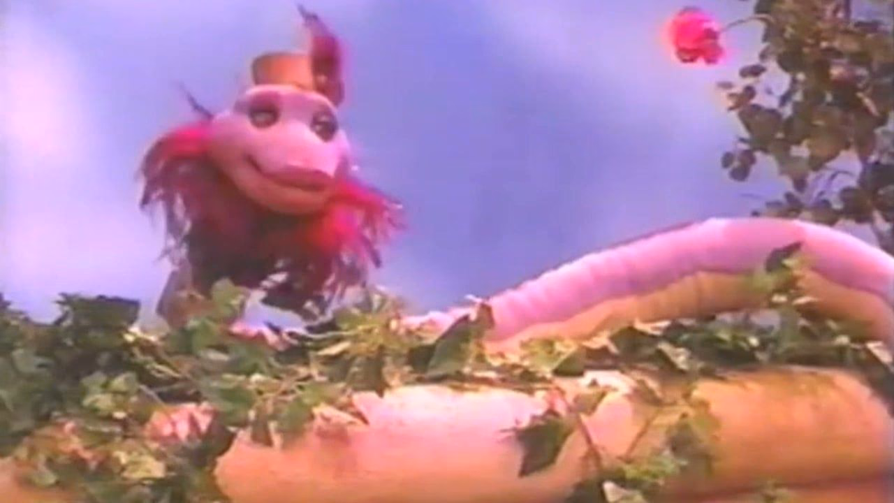 A pink snake puppet in a top hat among the garden set's foliage